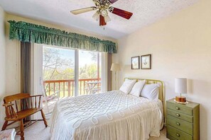 A bedroom with a bed, a nightstand, a chair, a balcony, and a ceiling fan.
