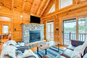 Ein Holzblockhaus-Interieur mit Kamin aus Stein, Holzwänden, einer Couch und einem Fernseher.