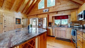 A wooden cabin interior with a kitchen featuring a marble countertop, wooden cabinets, and a stainless steel refrigerator. - Lakefront Cabin & Cozy Lakeview Cottage: firepit, wet bar, dock (Mills River)