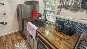 Una cucina con frigorifero in acciaio inossidabile, una valigia rossa, una macchina da caffè e una finestra con vista sul verde.