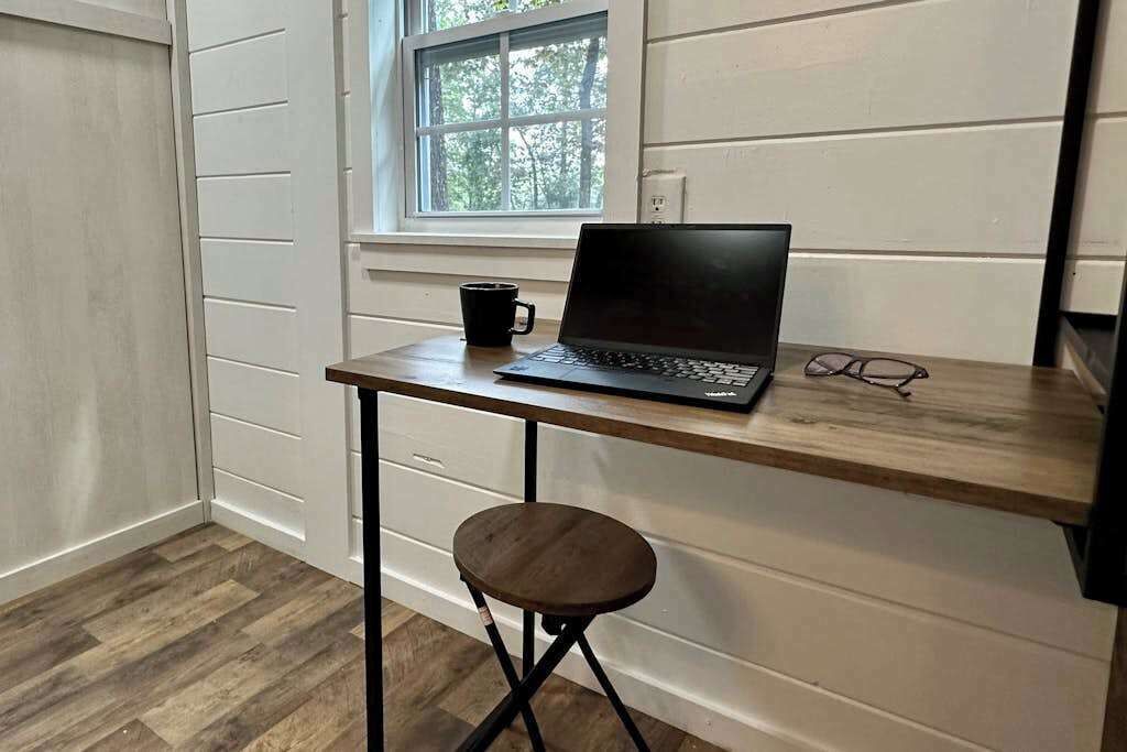 Et lille arbejdsområde med en bærbar computer, en kop og briller på et træbord.