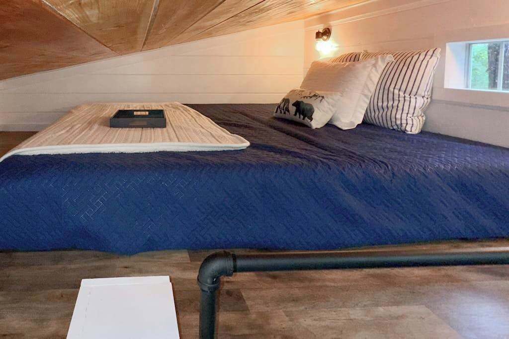 A bedroom with a sloped ceiling, a bed with a blue bedspread, a bedside table, and a window.