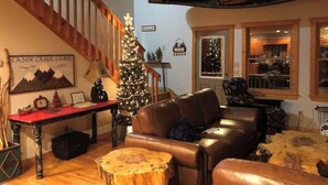 Ein gemütliches Blockhaus-Interieur mit einer Ledersofa, einem Holztisch, einem Weihnachtsbaum und einer Treppe.