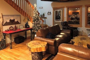 Ein gemütliches Blockhaus-Interieur mit einer Ledersofa, einem Holztisch, einem Weihnachtsbaum und einer Treppe.