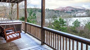 Eine Holzterrasse mit Schaukelstuhl mit Blick auf einen See und Hügel.