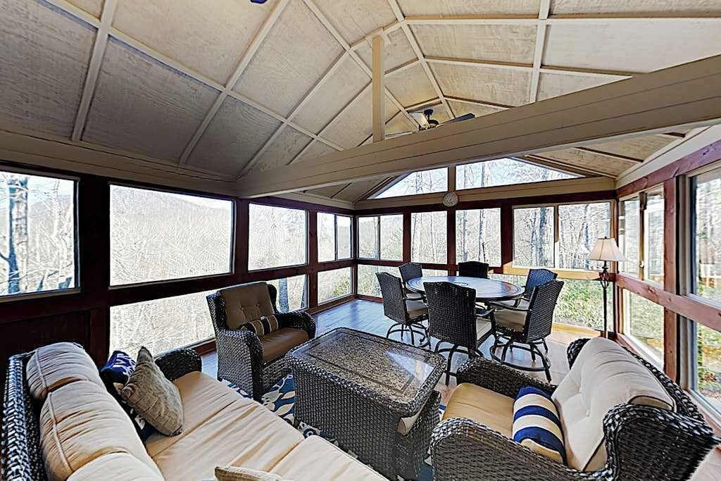 Une véranda avec des meubles en osier, de grandes fenêtres et un ventilateur de plafond.