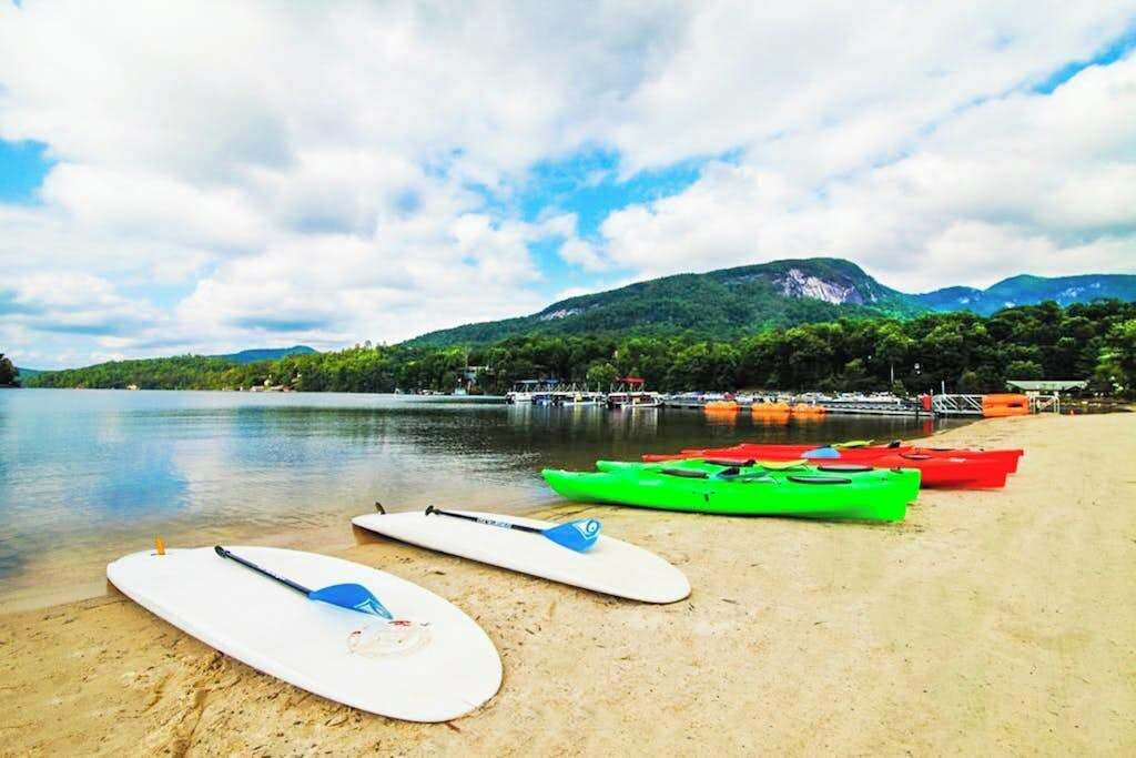 Une plage avec des kayaks et un lac paisible, entourée de verdure et de montagnes.