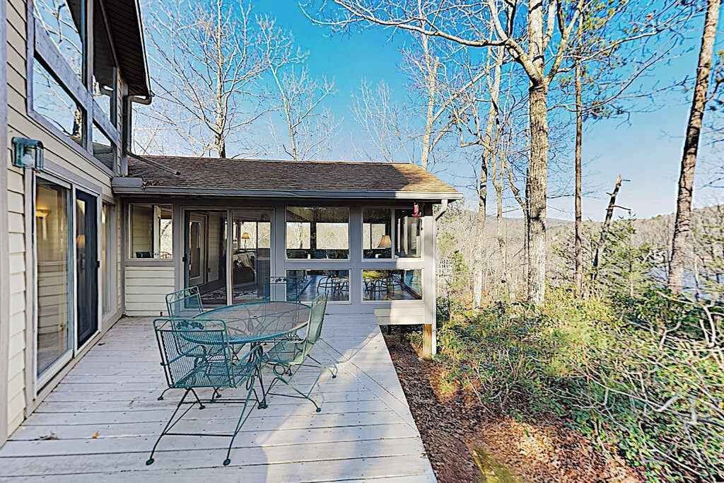 Un patio abrité avec une table et des chaises en verre, une terrasse en bois et une vue sur les arbres et les collines.