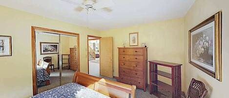 Une chambre à coucher avec un lit, une commode, une chaise et un ventilateur de plafond.
