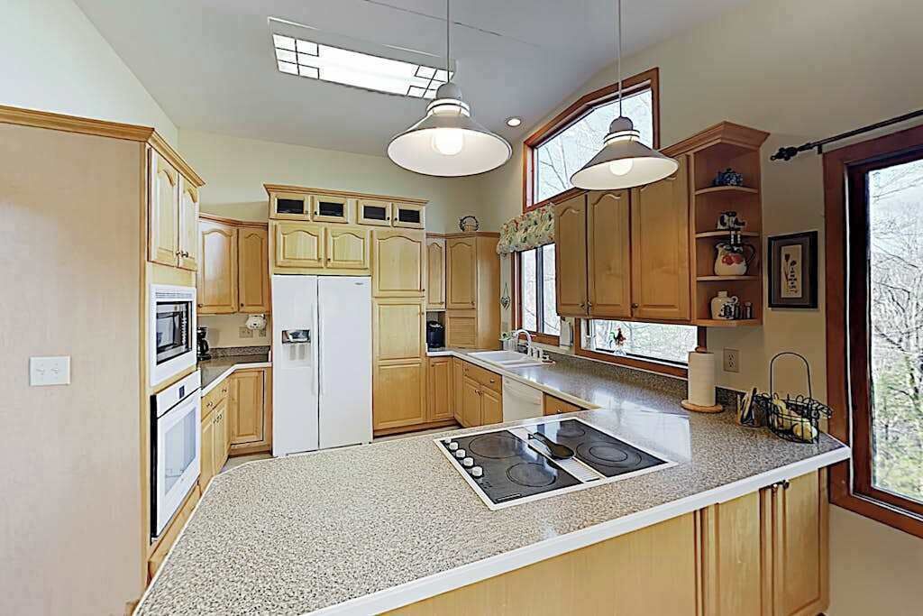 A kitchen with wooden cabinets, a central island with a stove, pendant lighting, and a view of the outdoors.