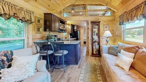 Interno di una baita con cucina, sala da pranzo e soggiorno, caratterizzato da pareti e soffitto in legno, un angolo bar e ampie finestre.