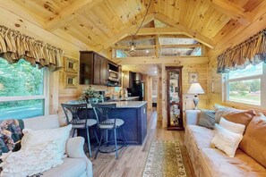 A cabin interior with a kitchen, dining area, and living room, featuring wooden walls and ceiling, a bar area, and large windows. - Cozy cabin with amazing views, private hot tub, & covered porch. Nearby skiing. (Mars Hill)