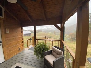 A wooden porch with a wicker sofa and a potted plant. - Cozy cabin with amazing views, private hot tub, & covered porch. Nearby skiing. (Mars Hill)