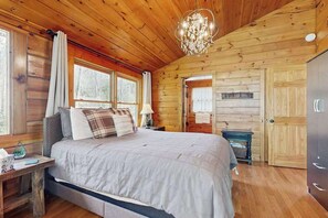 Dormitorio de una cabaña de madera con cama, mesitas de noche, un candelabro y una puerta.