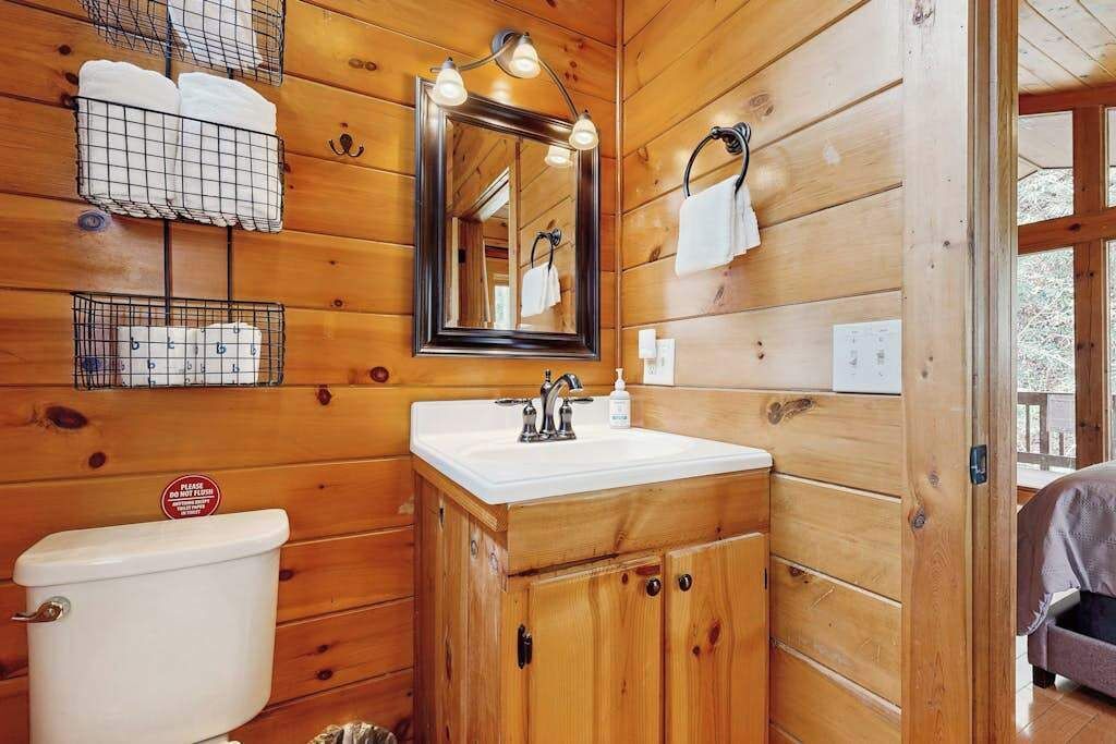 A wooden cabin bathroom with a toilet, sink, mirror, and towel racks.