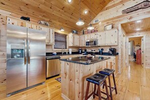 A kitchen with wooden cabinets, a stainless steel refrigerator, a microwave, and a bar stool. - Highlands Water Hideaway (Murphy)