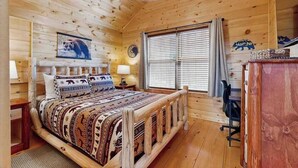 Ein Schlafzimmer in einer Holzhütte mit einem Bett, Nachttischlampen, einer Uhr, einem Fenster mit Jalousien und einer Bär-Motiv-Wanddekoration.