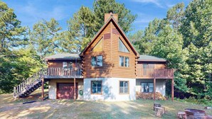 A two-story log cabin with a balcony, a staircase, and a fire pit in the yard.