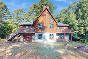 Eine zweistöckige Blockhütte mit Balkon, einer Treppe und einem Feuerkorb im Hof.