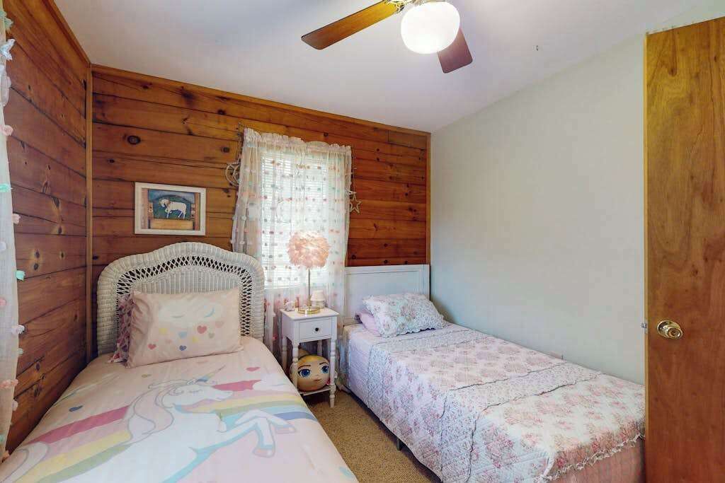 A bedroom with two beds, wooden walls, a ceiling fan, a nightstand, and a framed picture on the wall.