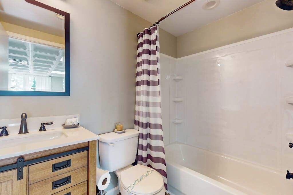A bathroom with a shower, toilet, sink, and mirror.