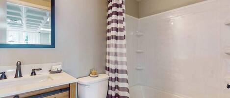 A bathroom with a shower, toilet, sink, and mirror.