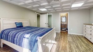 A bedroom with a bed, a dresser, a vanity, and a ceiling with skylights.