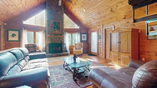 A log cabin interior with a high ceiling, a fireplace, leather sofas, and a stone pillar.