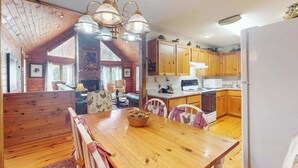 A cozy kitchen with wooden cabinets, a dining table with chairs, and a hanging light fixture.