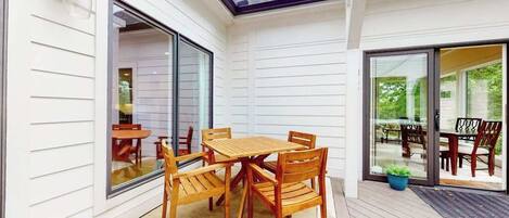 Eine überdachte Terrasse mit Holztisch und -stühlen, großen Schiebeglastüren und einem Blumentopf.