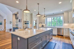 A modern kitchen with a large island, pendant lighting, and a view of the outdoors. - Mountain & lake-view luxury home with hot tub, deck, & pergola - dog-friendly (Mill Spring)