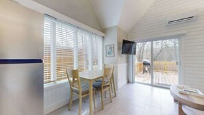 Una habitación con una mesa de comedor, sillas, un televisor montado en la pared y un ventanal corredizo que da a una terraza exterior.
