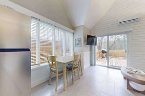 Ein Zimmer mit Esstisch, Stühlen, einem an der Wand befestigten Fernseher und einer Glastür zu einer Terrasse.