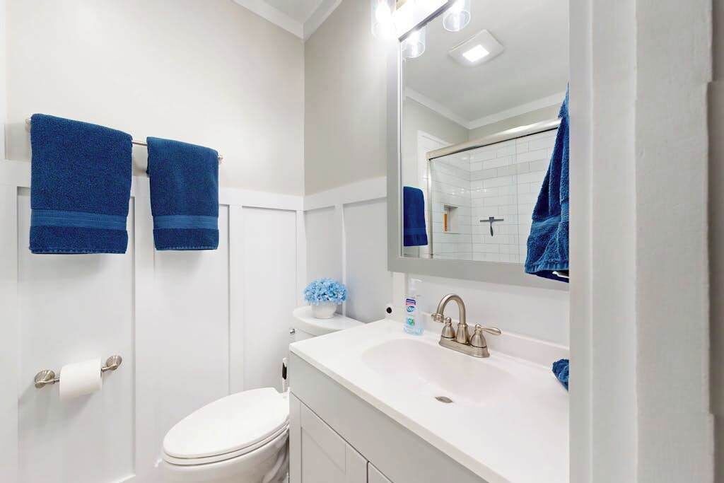 Un baño con un lavamanos blanco, un espejo y dos toallas azules colgadas en la pared.