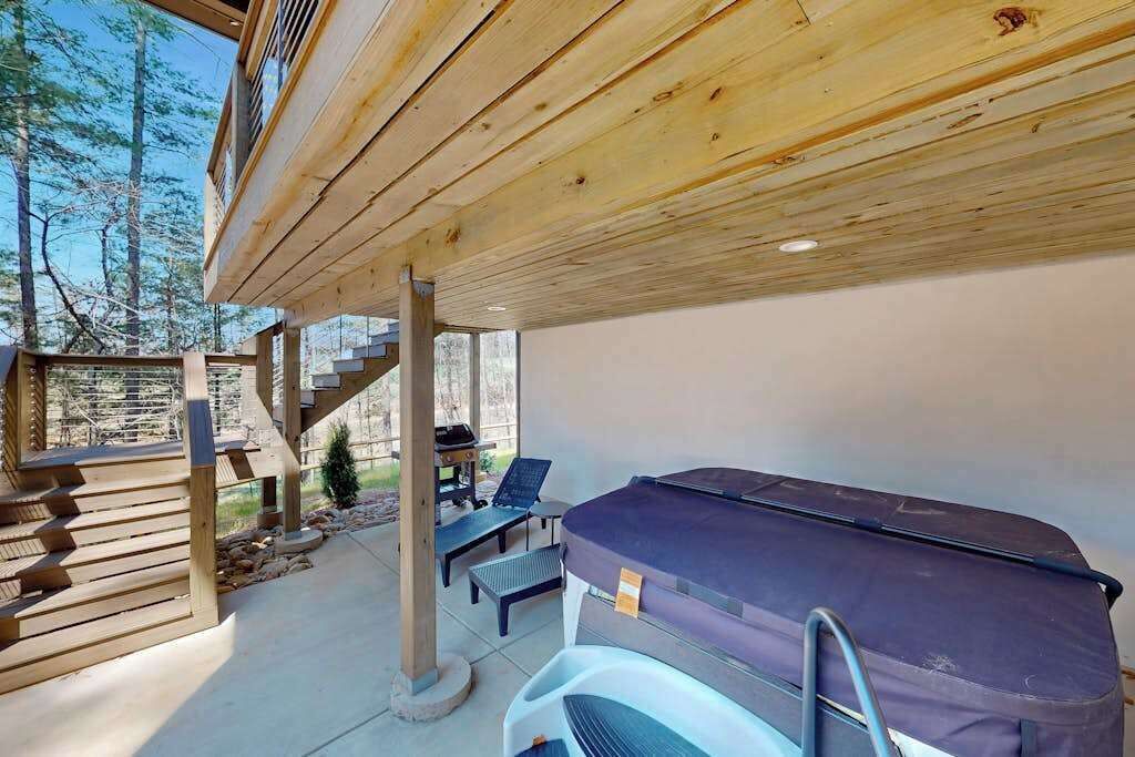 Un espacio al aire libre techado con un jacuzzi, sillas de descanso y una escalera que conduce a un nivel superior.