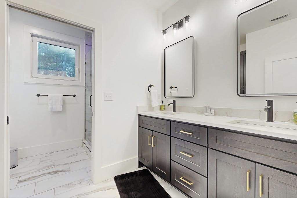 A modern bathroom with a large mirror, dark wooden cabinets, a white countertop, and a glass shower enclosure.