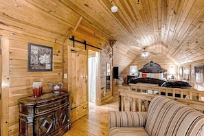 Ein rustikales Blockhaus-Interieur mit Holzbalkendecke, einem Bett, einer Couch und einem Schrank mit Dekorationen.