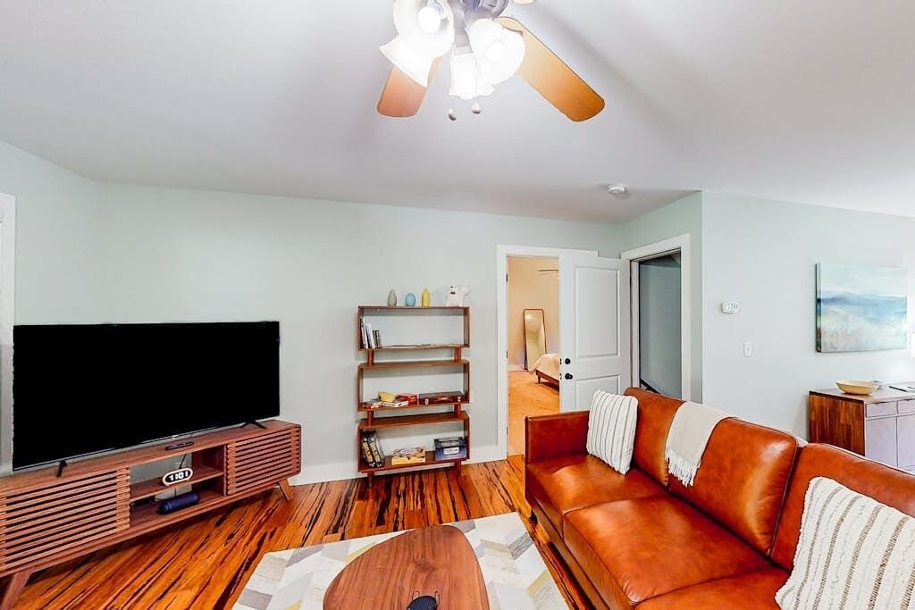 A living room with a TV, wooden entertainment unit, brown leather sofa, and a ceiling fan.