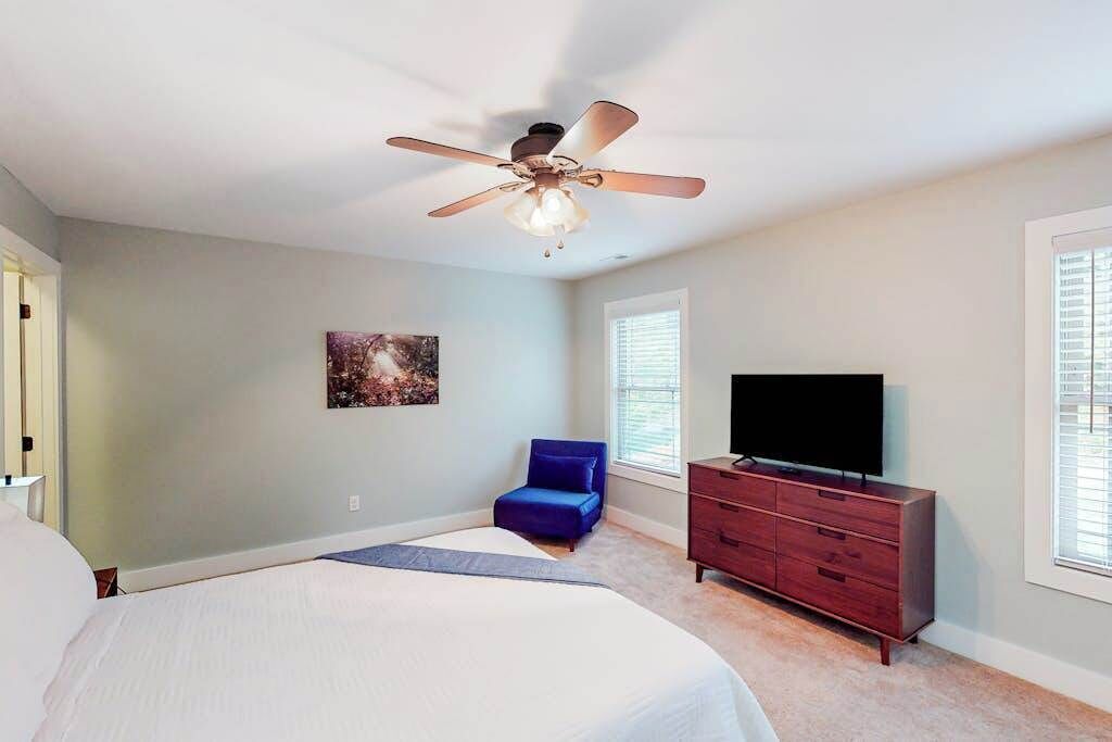 A bedroom with a bed, a ceiling fan, a dresser, a television, and a window.
