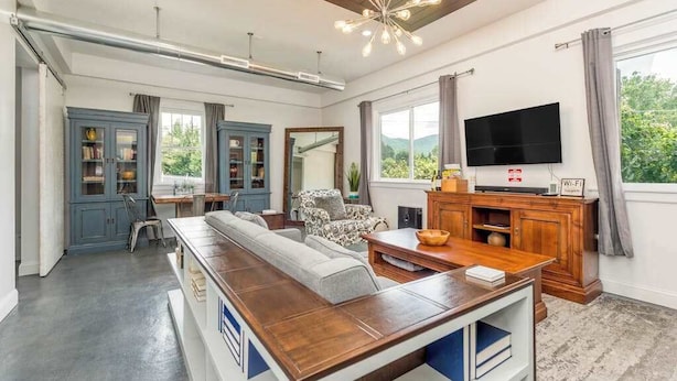 A modern living room with a long wooden table, a sofa, a television, and a cabinet. - Idyllic home with 2 separate apartments near skiing/hiking - firepit, fast WiFi (Swannanoa)
