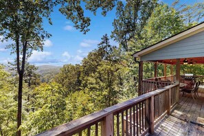 A wooden deck with a table and chairs, surrounded by trees and a mountainous landscape. - Rustic Lake Lure retreat with wifi, custom charm, lake fun & mountain views (Lake Lure)