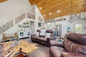A spacious living area with a brown leather sofa, a wooden coffee table, and a staircase leading to an upper level. - Rustic Lake Lure retreat with wifi, custom charm, lake fun & mountain views (Lake Lure)