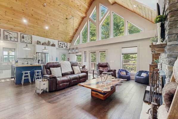 A spacious living area with a wooden ceiling, a leather sofa, a coffee table, and a stone fireplace. - Rustic Lake Lure retreat with wifi, custom charm, lake fun & mountain views (Lake Lure)