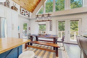 A spacious kitchen with a wooden dining table, a bench, and a large window overlooking greenery. - Rustic Lake Lure retreat with wifi, custom charm, lake fun & mountain views (Lake Lure)