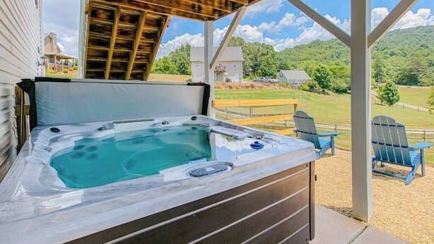 A hot tub under a wooden pergola with a view of a grassy landscape and houses. - Blue Ridge farmhouse with amazing mountain view, hot tub, firepit & decks (Weaverville)
