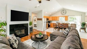 A spacious living room with a fireplace, a ceiling fan, and a kitchen in the background. - Blue Ridge farmhouse with amazing mountain view, hot tub, firepit & decks (Weaverville)