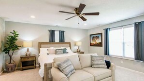 A bedroom with a bed, a ceiling fan, a nightstand, a lamp, a window with curtains, a plant, and a painting on the wall. - Blue Ridge farmhouse with amazing mountain view, hot tub, firepit & decks (Weaverville)
