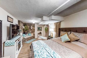 Ein Schlafzimmer mit Steinwand, einem Bett mit gemusterten Bettbezügen, einem Fernseher und einem kleinen Tisch mit Lampe.