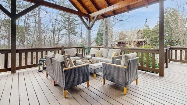 Una terraza techada al aire libre con mobiliario de mimbre, techo de madera y vistas a árboles y una casa al fondo.