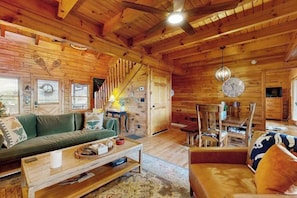 Ein Holzblockhaus im Inneren mit einer Couch, einem Couchtisch, einem Esstisch, Stühlen und einer Treppe.